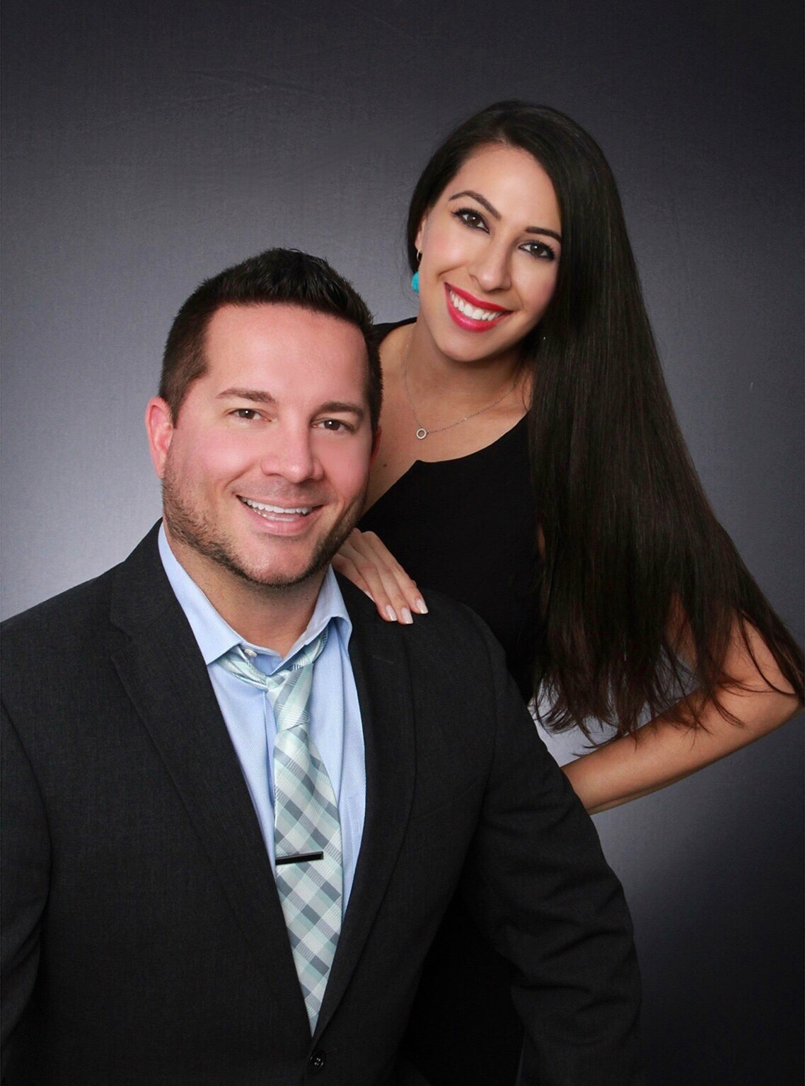 Justin and Alyse Keller of The Keller Team at Compass posed together in a studio portrait, Justin in a dark suit and Alyse in a black top